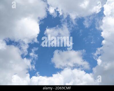 Looking up at patch of blue sky surrounded by white clouds Stock Photo