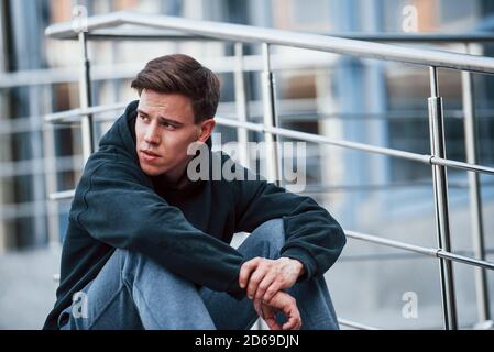 Portrait of young main in black clothes that sits on the stairs and taking a break Stock Photo