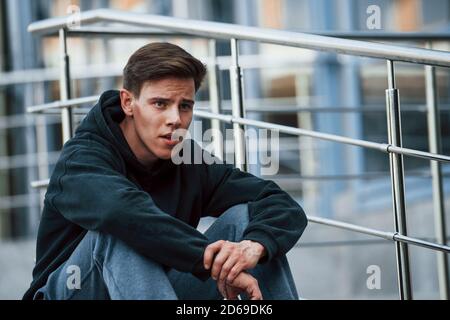 Portrait of young main in black clothes that sits on the stairs and taking a break Stock Photo