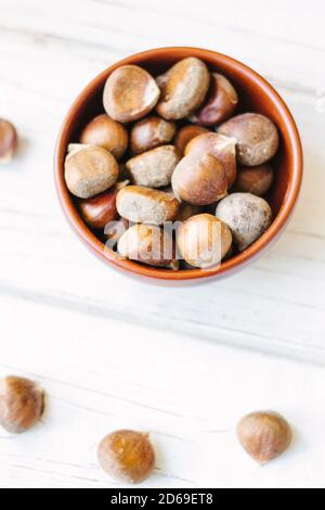 Raw chestnuts in ceramic bowl on white surface. Stock Photo