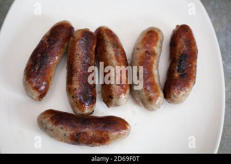 Half a dozen cooked British pork sausages on a white plate Stock Photo