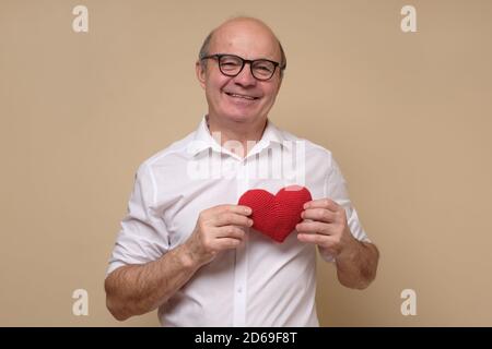 Senior gentleman in glasses holding a red heart smiling. Stock Photo