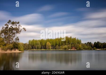 Long exposure view across a lake towards an island with a scandinavian style forest of birch trees and a log cabin Stock Photo