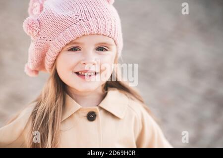 Smiling baby girl 2-3 year old wearing knitted hat and jacket outdoors close up. Childhood. Autumn season. Stock Photo
