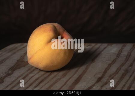 Still-life low-key shot of a peach fruit on a raw wooden surface Stock Photo