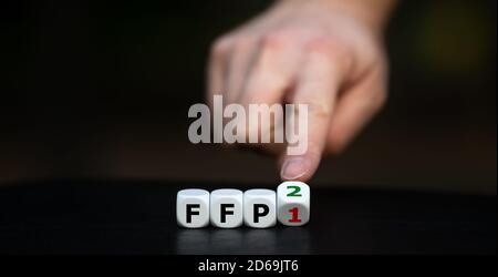 Symbol for wearing a FFP2 mask. Hand turns dice and changes the expression "FFP1" to "FFP2". Stock Photo