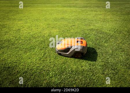 Automatic orange and grey lawn mower robot moves on the green grass, side view, photography. Stock Photo