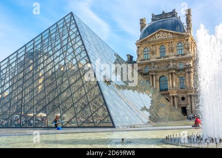 France, Paris. Summer sunny day in the courtyard of the Louvre Museum. Manual and automatic washing of the glass pyramid. Fountain and tourists.