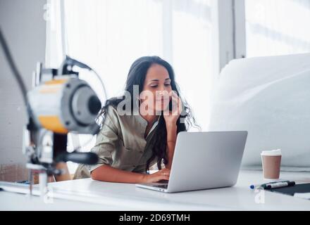 Using laptop. Beautiful female worker is in the sewing factory Stock Photo