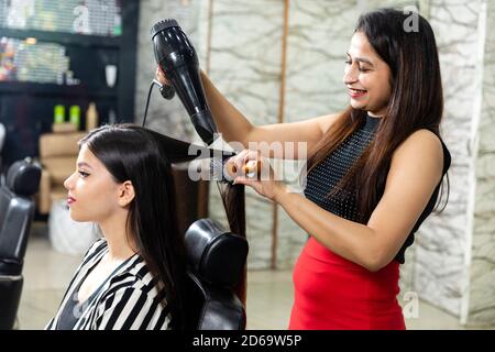 A hair dresser provides hair styling services to a pretty young Indian woman, beautiful woman gets her hair done at a salon, selective focus. Stock Photo