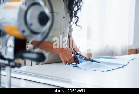 Female worker is in the sewing factory at daytime cutting cloth with scissors Stock Photo