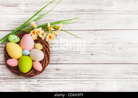 Happy Easter. Congratulatory easter background with copy space. Colorful Easter eggs in the nest and narcissus flowers on light wooden background. Stock Photo