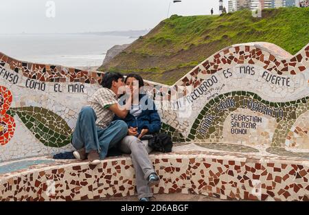 Miraflores, Peru - December 4, 2008: Parque del Amor, Love Park. Young kissing couple on artful mosaic bench with ocean and green cliff in background. Stock Photo