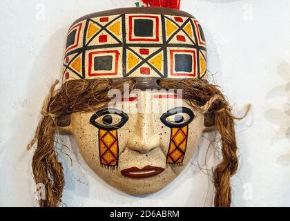 Lima, Peru - December 4, 2008: Closeup of colorful mask of female face with traditional hat and long hair with white wall as backdrop. Stock Photo