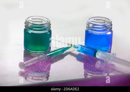 Closeup Photo of Blue and Green Liquid Glass Containers With Two Syrings Infront of Them with Purple Grain Shadow Stock Photo