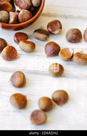 Brown chestnuts in bowl over white wooden surface. Stock Photo