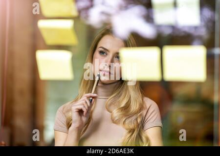 Young businesswoman brainstorming with notes on a glass wall in an office Stock Photo