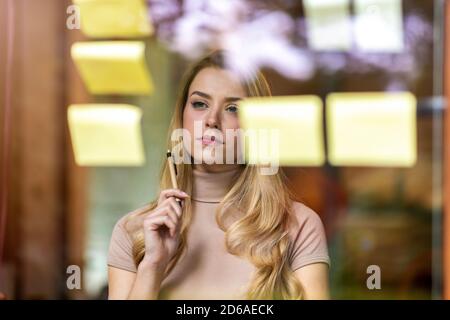 Young businesswoman brainstorming with notes on a glass wall in an office Stock Photo