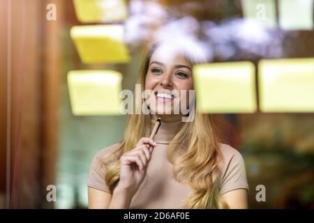 Young businesswoman brainstorming with notes on a glass wall in an office Stock Photo