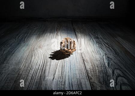 Abstract Christmas background with a pine cone highlighted by hard light surrounded by shadows on a natural wooden background. Stock Photo