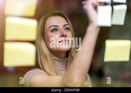 Young businesswoman brainstorming with notes on a glass wall in an office Stock Photo