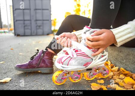 A girl puts on roller skates sitting on a concrete curb. Child fastens roller skates. Close up view, no face. Stock Photo