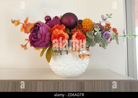 Artificial flowers in a white vase on a shelf in the room. Fabric flowers as an element of interior decor. Artificial peonies, a bouquet of flowers in Stock Photo