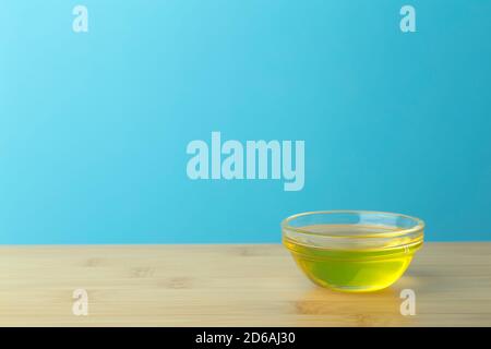 Oil in a glass bowl on a clean blue background. Cosmetic or food oil background. Copy space Stock Photo