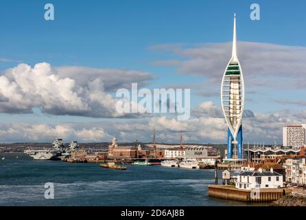the entrance to portsmouth harbour with the spinnaker tower and hms queen elizabeth under a sky full of summer clouds.