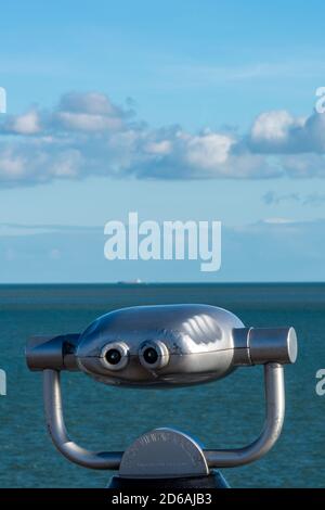 a retro style viewing telescope looking out to sea from the coastline or shoreline on the beach at the seaside. Stock Photo