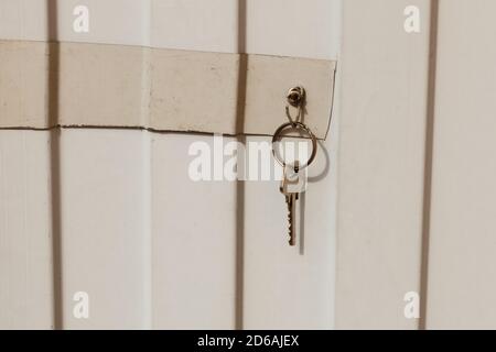 The key is hanging from a hook on a metal fence. The key to the door lock. Stock Photo