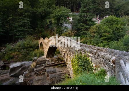 people empty rustic roman bridge in ticino, warm sunset, bright green forest with ticino stone houses, the famous bridge is a destination for many tou Stock Photo