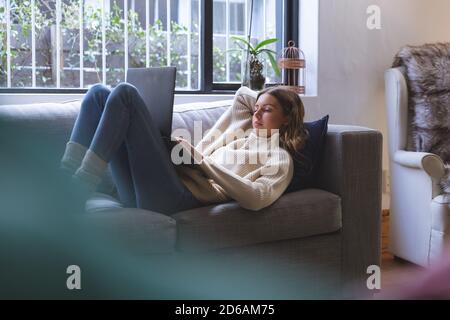 Woman using laptop while laying on couch at home Stock Photo