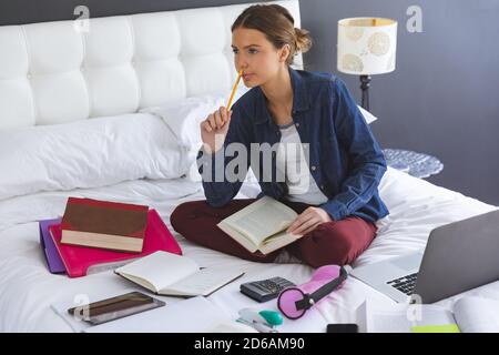 Thoughtful woman holding book while sitting on bed at home Stock Photo