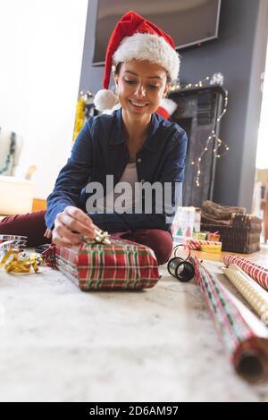 Woman in Santa hat wrapping Christmas presents at home Stock Photo