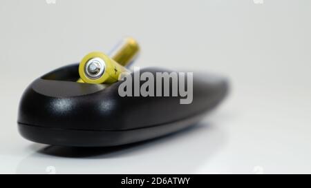 Black remote control with yellow AAA batteries on a white background. Battery replacement, spare parts. Remote control battery compartment close-up Stock Photo