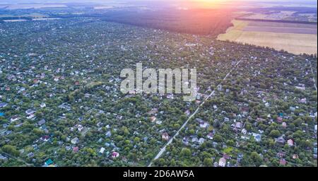 View of the suburban village on the outskirts of the city from a height at sunset. Plenty of private homes and homes in the green zone with small-density development - aerial shot. Stock Photo