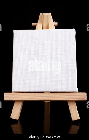 Small easel with white blank cloth on a wooden table. Miniature painting accessories. Dark background. Stock Photo