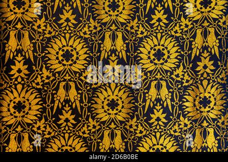 Closeup of a tapestry or fabric patern in gold and black with flowers and birds background backgrop Stock Photo