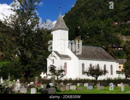 White Wooden Church With A Cemetery In The Foreground In Oystese Surrounded By Large Mountains On A Sunny Summer Day With A Clear Blue Sky And A Few C Stock Photo
