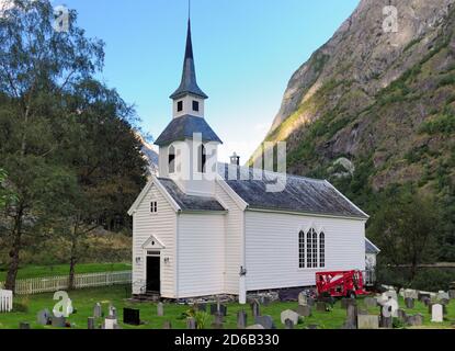 White Wooden Chapel Surrounded By Large Mountains In Undredal At Aurlandsfjord In The Late Afternoon On A Sunny Summer Day With A Clear Blue Sky And A Stock Photo