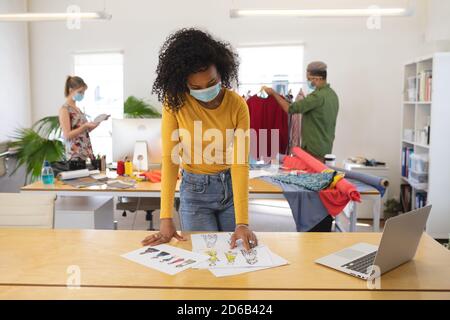 Female fashion designer wearing face mask looking at sketches of clothing design at studio Stock Photo