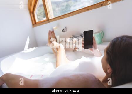 Woman using smartphone while relaxing in a bathtub Stock Photo
