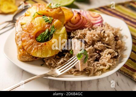 Marinated Cuban pineapple pork chops with traditional black bean rice grilled red onion and fried plantain chips Stock Photo