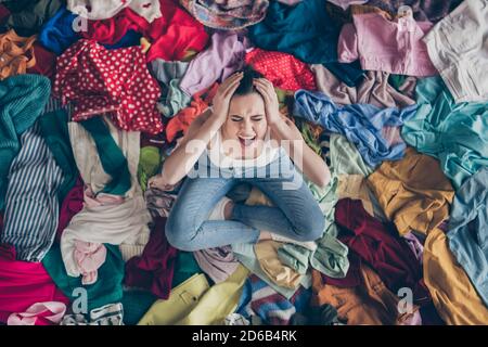 Help. High angle above view photo of stressed yelling lady stay home spring cleaning household sit many clothes stack floor pick select look outfit Stock Photo