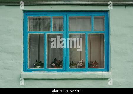 Blue wooden window of an old private house, whose walls are painted in light green color. The old building. Plastered walls. Stock Photo