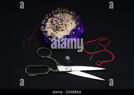 Needle bed, thimble, scissors, needle and thread on black fabric background. Stock Photo