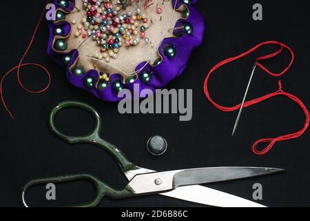 Needle bed, thimble, scissors, needle and thread on black fabric background. Stock Photo
