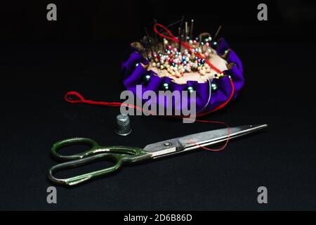 Needle bed, thimble, scissors, needle and thread on black fabric background. Stock Photo