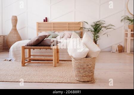Two white pillows in eco wicker basket on background cozy wooden bed with bedspread of pastel colors, pillows of powdery shades and blanket of delicat Stock Photo